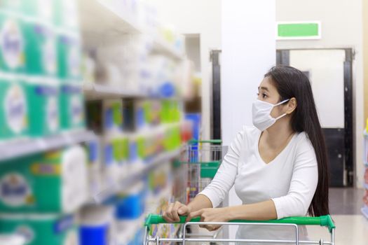 Asian woman wear face mask push shopping cart in supermarket. Girl looking grocery to buy something During coronavirus crisis or covid19 outbreak. Women wearing protective face mask new normal concept