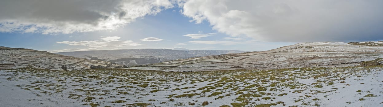 Panoramic view over an overcast snowy winter english countryside rural landscape with fields and meadows