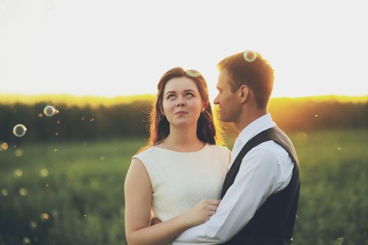 Happy bride and groom hug each other in the park at sunset. Soap bubbles. Wedding. Happy love concept. High quality photo