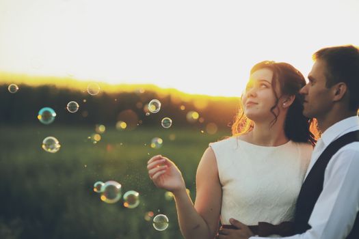 Happy bride and groom hug each other in the park at sunset. Soap bubbles. Wedding. Happy love concept. High quality photo