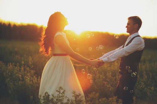 The bride and groom hold hands dancing in the park. Sunset light. Soap bubbles. Wedding. Happy family concept. High quality photo