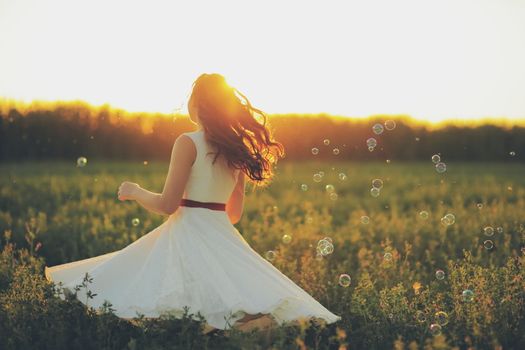 Beautiful girl dancing in a park in the sunset light. Soap bubbles. Happiness concept. High quality photo