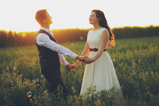 The bride and groom hold hands dancing in the park. Sunset light. Soap bubbles. Wedding. Happy family concept. High quality photo