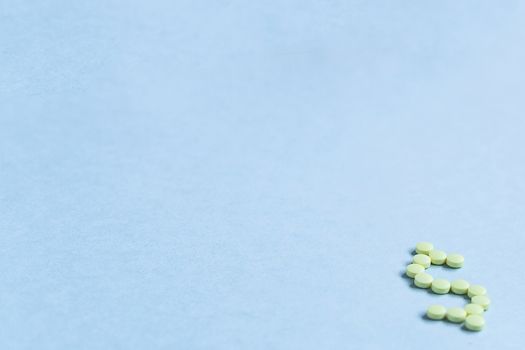 tablets in the form of a dollar sign on a blue background. Concept of a dollar sign made with vitamin tablets on a blue background.banner. copy space. soft focus, blurry background. space for text.