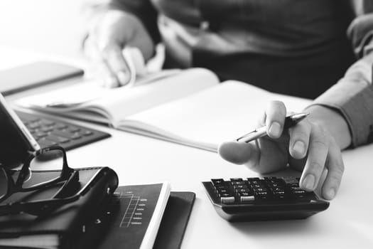 businessman hand working with finances about cost and calculator and latop with mobile phone on withe desk in modern office,black and white