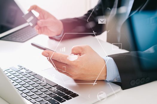 businessman making credit card purchase online with mobile phone and laptop computer on modern desk with VR icon diagram