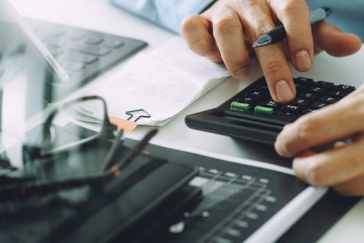 close up of businessman hand working with finances about cost and calculator and latop with mobile phone on withe desk in modern office 