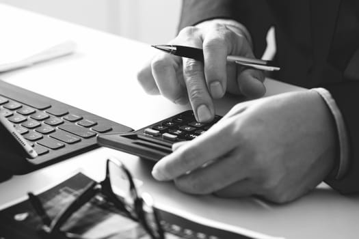 close up of businessman hand working with finances about cost and calculator and latop with mobile phone on withe desk in modern office,black and white