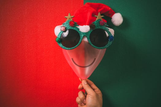 Hand holding Christmas glasses that decoration with Christmas tree and red hat on air bolloon   on green background