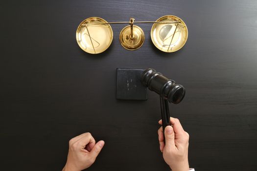 justice and law concept.Top view of Male judge hand in a courtroom with the gavel and brass scale on dark wood table