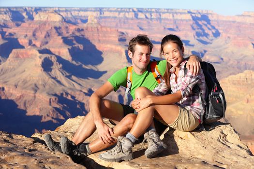 Hiking couple portrait - hikers in Grand Canyon enjoying view of nature landscape looking at camera smiling happy. Young couple trekking, relaxing after hike on south rim of Grand Canyon, Arizona, USA