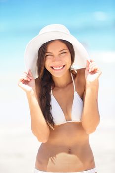 Beach woman happy and playful smiling laughing playful and cheerful in summer sun. Beautiful multiracial Asian Chinese / Caucasian woman wearing white beach hat and bikini.