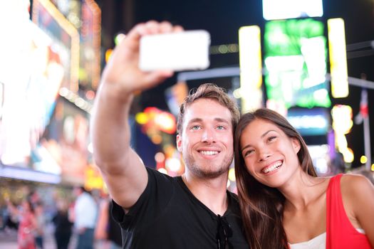 Dating young couple happy in love taking selfie self-portrait photo on Times Square, New York City at night. Beautiful young tourists having fun date, Manhattan, USA. Asian woman, Caucasian man