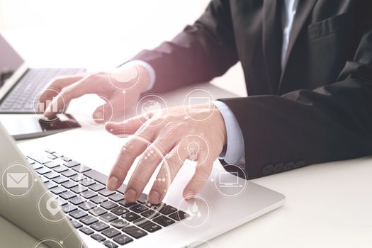 Hands of businessman typing on laptop in modern office with smart phone and digital tablet computer with VR icon diagram