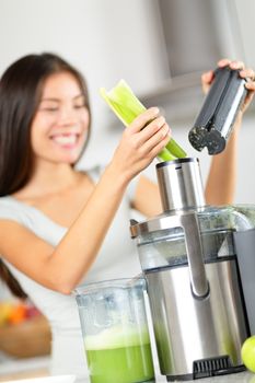 Vegetable juice - woman juicing green vegetables on juicer machine or juice maker. Healthy raw food concept with person making celery vegetable juice in kitchen. Focus on celery.