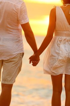 Romantic couple holding hands on beach sunset during travel. Happy woman and man in romance on honeymoon romance in beautiful sun light.