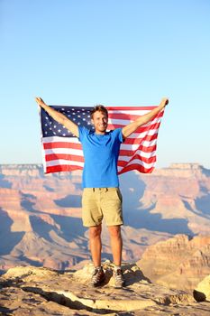 American USA flag - tourist in Grand Canyon. Happy young man hiking and cheering at Grand Canyon south rim during summer holidays in the United States. Young male hiker in his 20s.