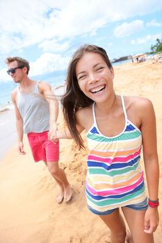 Beach people. Young interracial happy playful couple holding hands walking on beach having fun on travel vacation - woman smiling laughing man in background . Asian woman, Caucasian man on Big Island, Hawaii, USA.