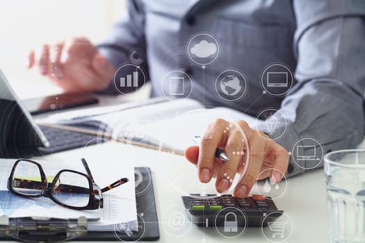 businessman hand working with finances about cost and calculator and latop with mobile phone on withe desk in modern office with VR icon diagram