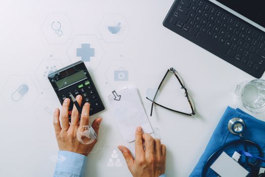 top view of Healthcare costs and fees concept.Hand of smart doctor used a calculator for medical costs in modern hospital with VR icon diagram