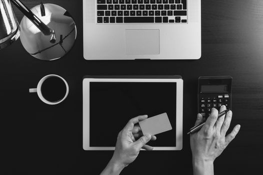 Internet shopping concept.Top view of hands working with calculator and laptop and credit card and tablet computer on dark wooden table background,black and white