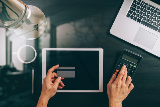Internet shopping concept.Top view of hands working with laptop and credit card and tablet computer on dark wooden table background