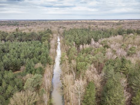 Aerial drone shot, of a forest with river or canal running through in early spring. Location: antitankgracht Kapellen. Creative edit.