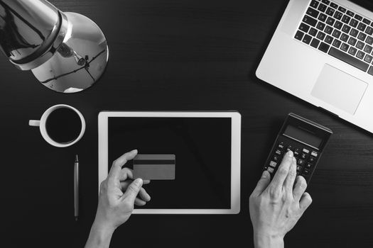 Internet shopping concept.Top view of hands working with laptop and credit card and tablet computer on dark wooden table background,black and white