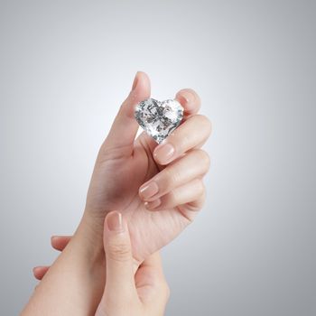 hand holding 3d heart shape of diamond over grey background