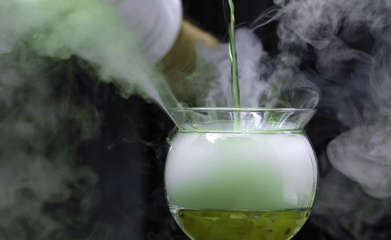Making Grape Martini Cocktail. Close up bartenders hands pouring green martini into a glass. The glass is wrapped in steam