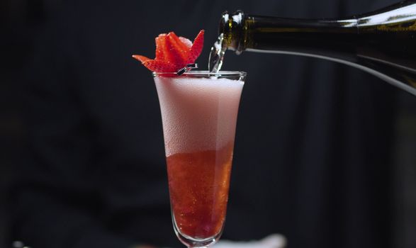 Making Strawberry Rossini Cocktail. Close up bartenders hands pouring champagne into a glass with crushed strawberries.