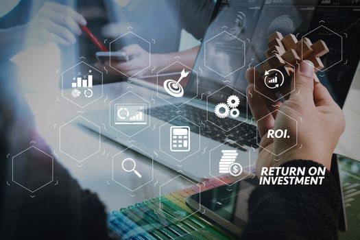 ROI Return on Investment indicator in virtual dashboard for improving business. two colleague web designer discussing data and digital tablet and computer laptop with smart phone and design diagram on marble desk.