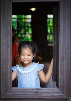 happy little asian girl standing by the window