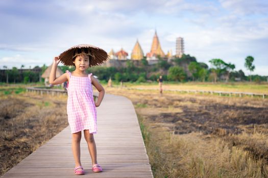 Portrait of happy asian little girl wear hat  in dress standing on bridge footpath with temple background