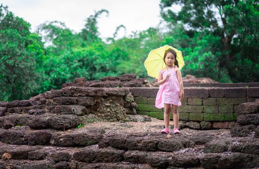 Little asian girl with yellow umbrella standind on th rock of historic site in Thailand