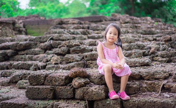 Little asian girl sitting on th rock of historic site in Thailand