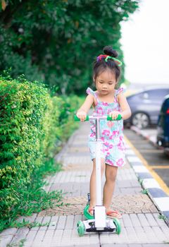 Cute little asian girl learning to ride a scooter on footpath
