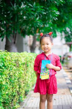 Portrait of happy asian little girl in red dress standing on footpath in the park