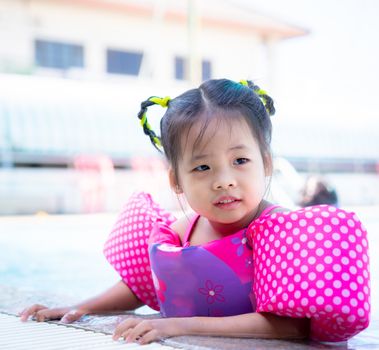 little asian girl wearing inflatable sleeves swimming in the pool
