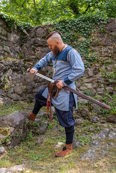 Viking warrior draws his sword, full-length profile portrait of a man in medieval clothes