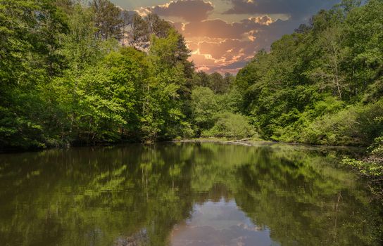 A Calm Lake in Green Forest Under Sunset Sky Reflected