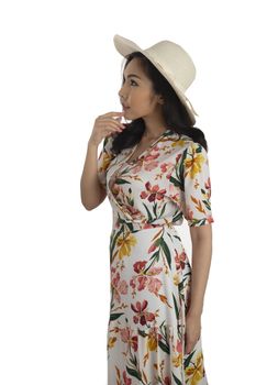 Side photo of pretty girl wearing floral dress with white straw hat standing on white background.