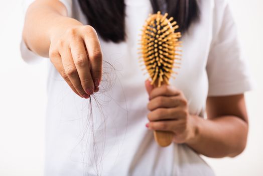 Asian woman unhappy weak hair problem her hold hairbrush with damaged long loss hair in the comb brush she pulls loss hair from the brush, isolated on white background, Medicine health care concept