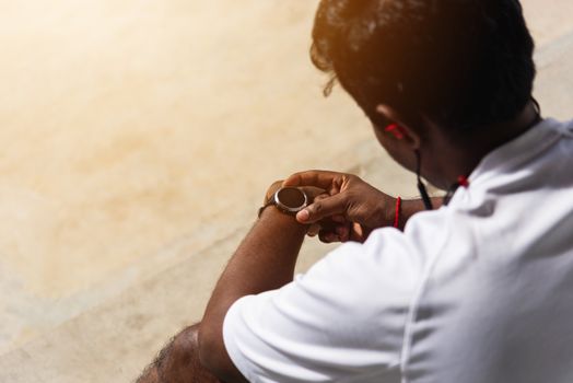 Close up Asian young athlete sport runner black man wear modern time smart watch he sitting resting before training running at the outdoor street health park, healthy exercise before workout concept