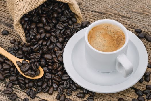 Coffee cup and coffee beans roasted in a sack on a wooden floor.