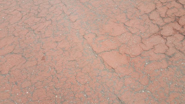 Red colored damaged road or paved pathway with crackes of different shpaes. Cracked texture with copy space for text and messages