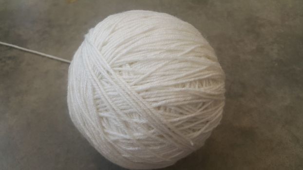 Off white ball of threads wool yarn for knitting on grey floor background