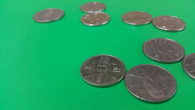 Silver shining Korean won coin scattered over a green floor.