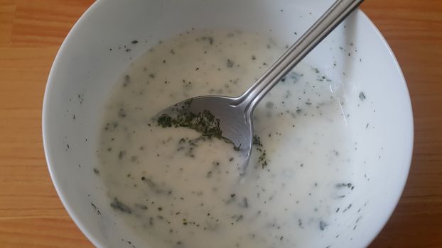 Close up of plain curd or yogurt or dahi in white ceramic bowl with silver spoon on a wooden surface. Curd is a dairy product obtained by coagulating milk in a process called curdling