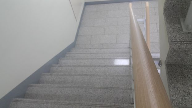 Closeup view of wooden handrail of grey concrete stairs in a modern building. Handrails help people avoiding accidents while moving on stairs.